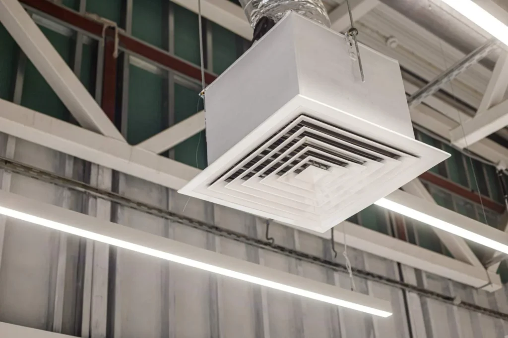 A close-up of a square grid supply ventilation duct in a commercial ceiling, illustrating the airflow mechanics behind how does an air purifier work to circulate clean air.