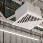 A close-up of a square grid supply ventilation duct in a commercial ceiling, illustrating the airflow mechanics behind how does an air purifier work to circulate clean air.