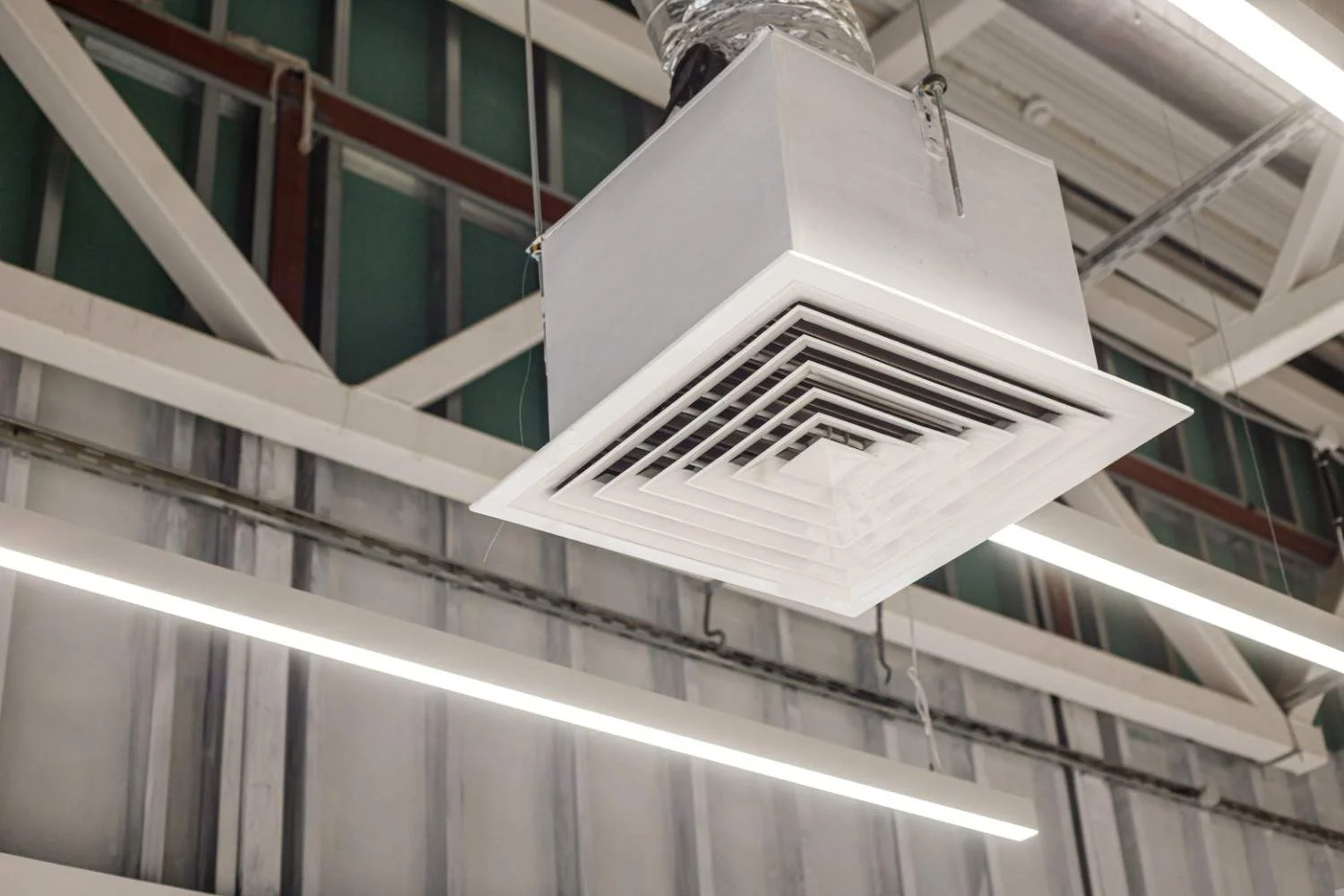 A close-up of a square grid supply ventilation duct in a commercial ceiling, illustrating the airflow mechanics behind how does an air purifier work to circulate clean air.