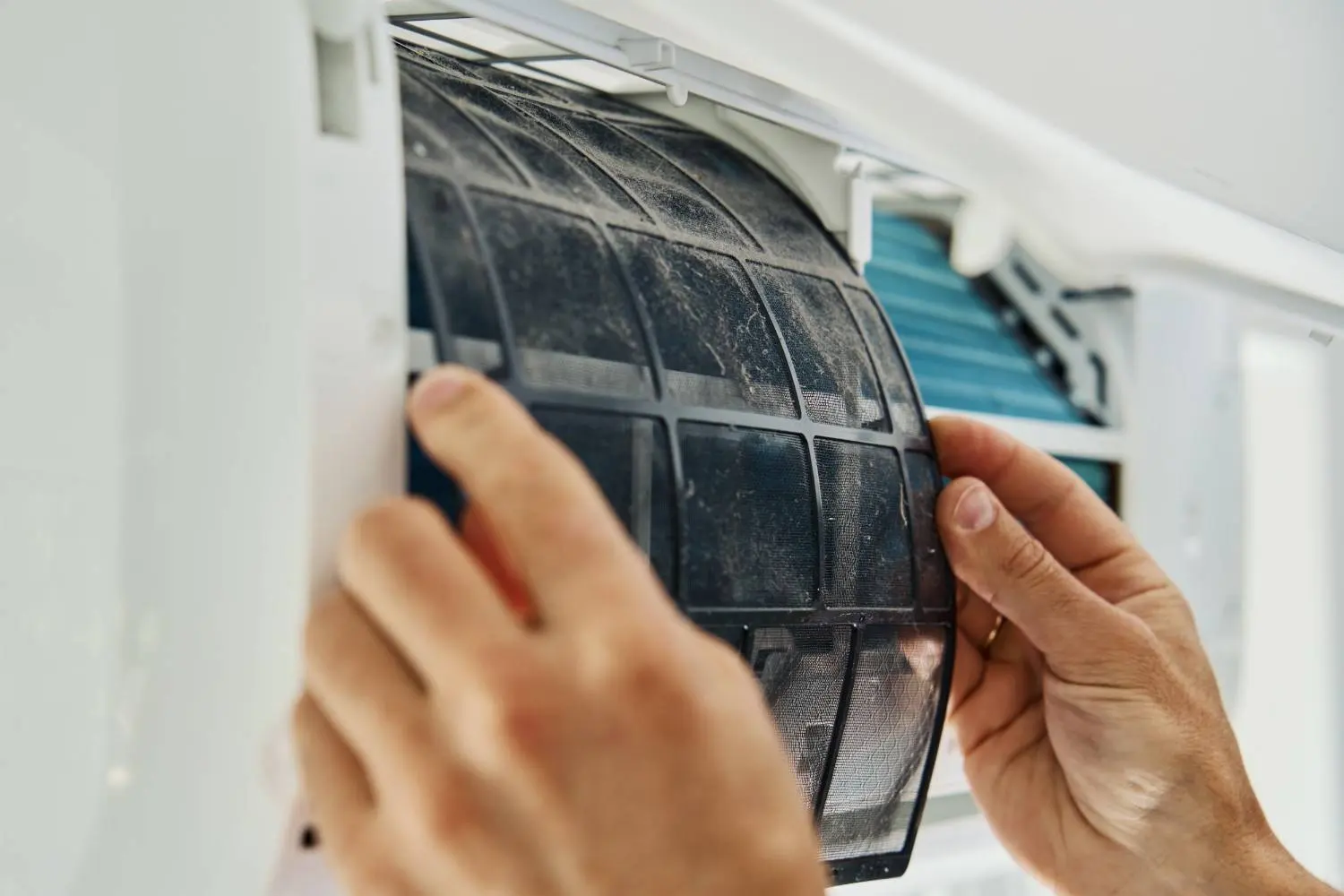 Hands removing a dusty, clogged mesh filter from an AC unit, showcasing the typical airborne particles to answer what pollutants do air purifiers remove from indoor spaces.