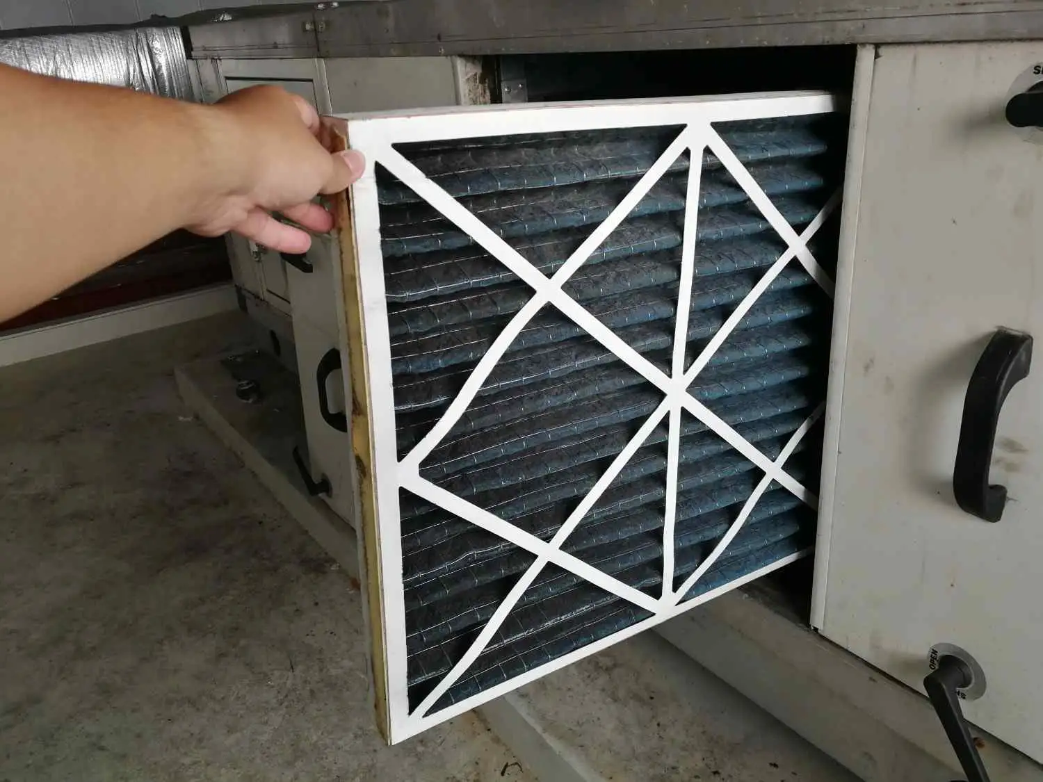 A technician slides a thick, pleated air filter into an air handling unit, illustrating the common question: can a high MERV filter damage your furnace by restricting airflow?