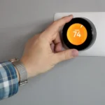 A man's hand adjusting a smart thermostat on a wall, illustrating the question: can nest thermostat