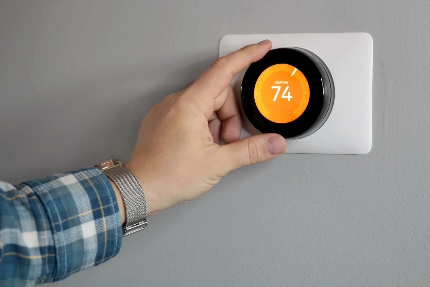 A man's hand adjusting a smart thermostat on a wall, illustrating the question: can nest thermostat replace heating and air conditioning?