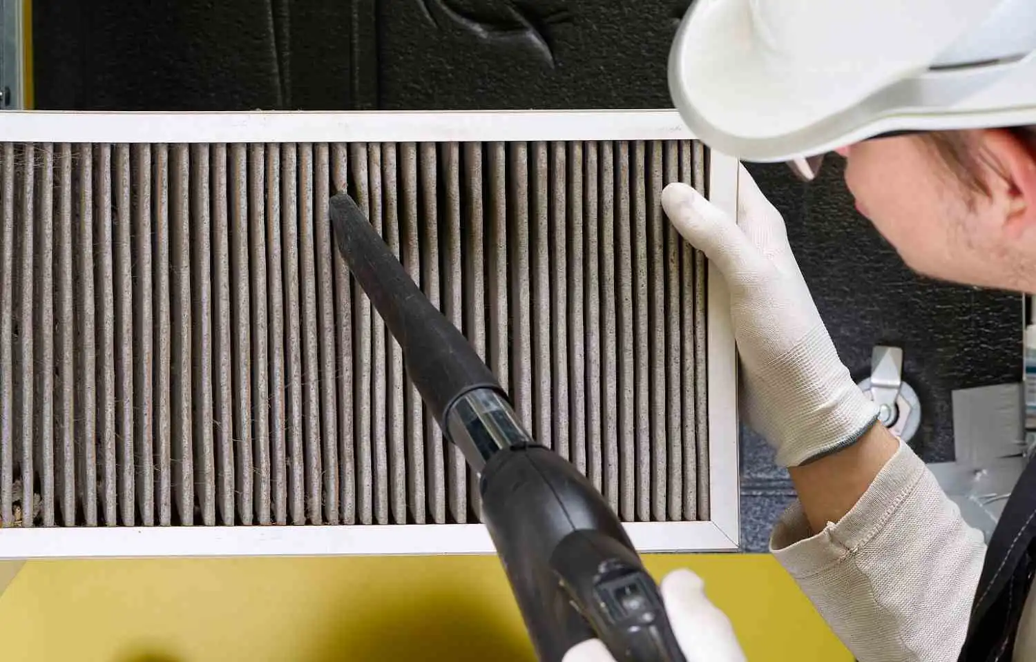 Person vacuuming a dirty air filter attachment to explore can you clean air ducts yourself at home.