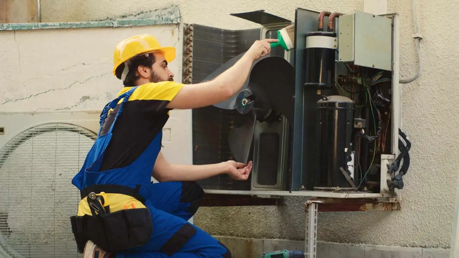 An HVAC technician using a brush to clean dust and debris from an outdoor air conditioner condenser fan, preventing restricted airflow which is one of the primary causes of HVAC static pressure issues.
