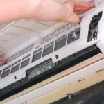 A technician opening the front panel of an indoor AC unit to troubleshoot common problems with mini splits.