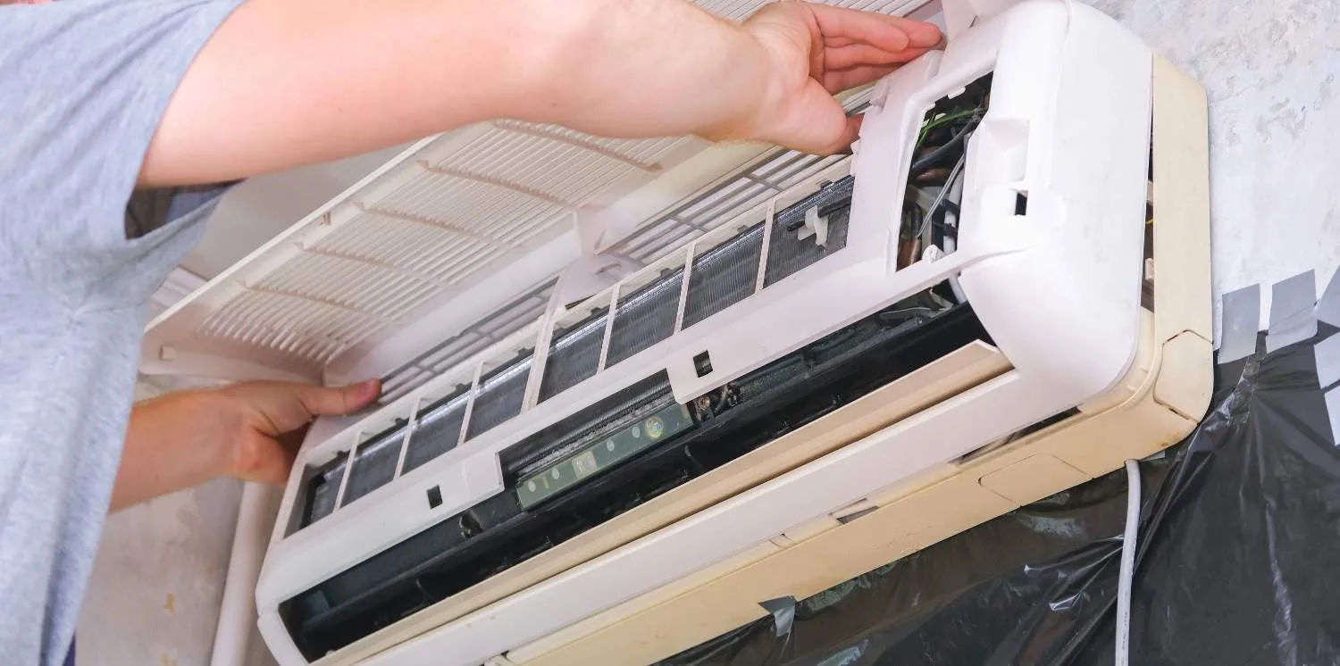 A technician opening the front panel of an indoor AC unit to troubleshoot common problems with mini splits.