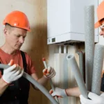 Two professional technicians in hardhats preparing pipe insulation during a guide on how to install a gas furnace.