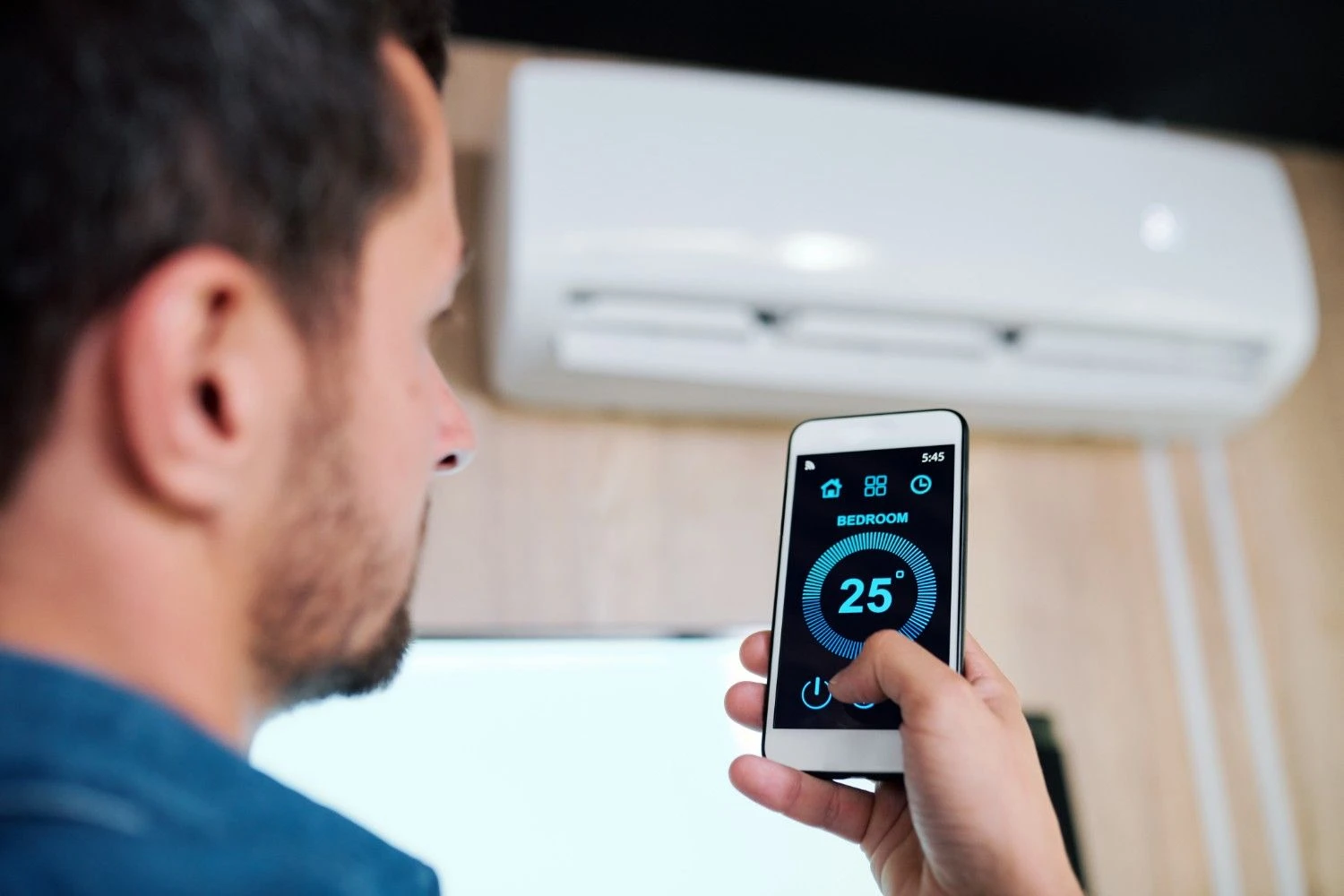A man using a smartphone app to control a ductless air conditioner unit, highlighting information for the section Mini-Split Systems and Nest: A Quick Note.
