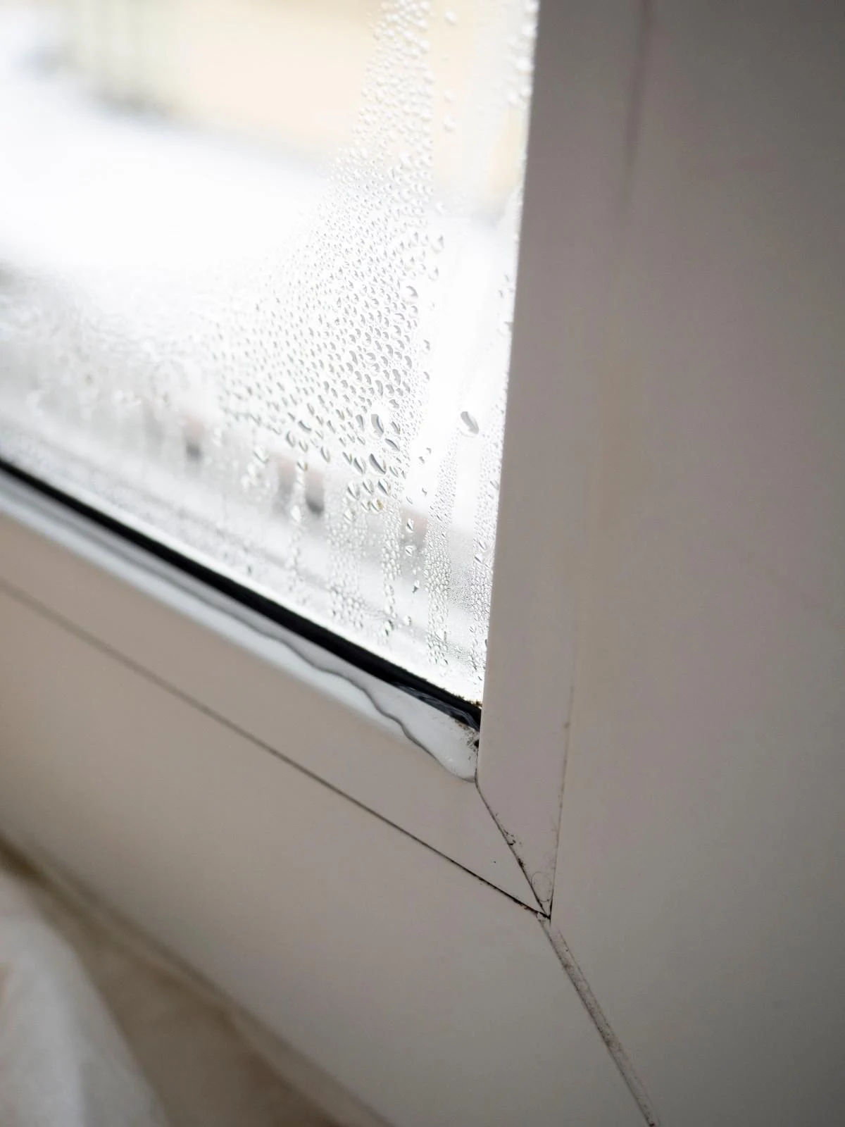 A close-up of heavy water condensation droplets on an indoor glass window pane, illustrating classic signs your AC isn't dehumidifying properly.