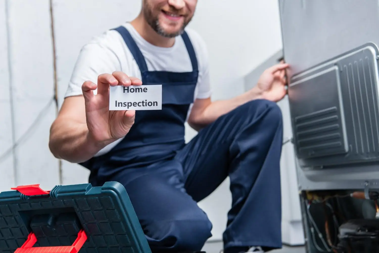 A smiling professional technician holding up a "Home Inspection" card while kneeling next to an appliance, illustrating the crucial steps when identifying signs your furnace needs repair or replacement.