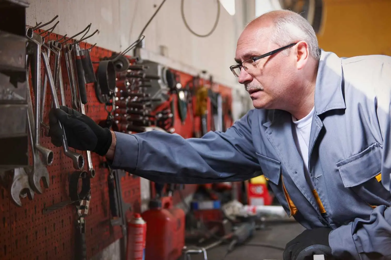 An experienced mechanic in a workshop selecting a wrench from a pegboard displaying the tools & equipment professionals use.