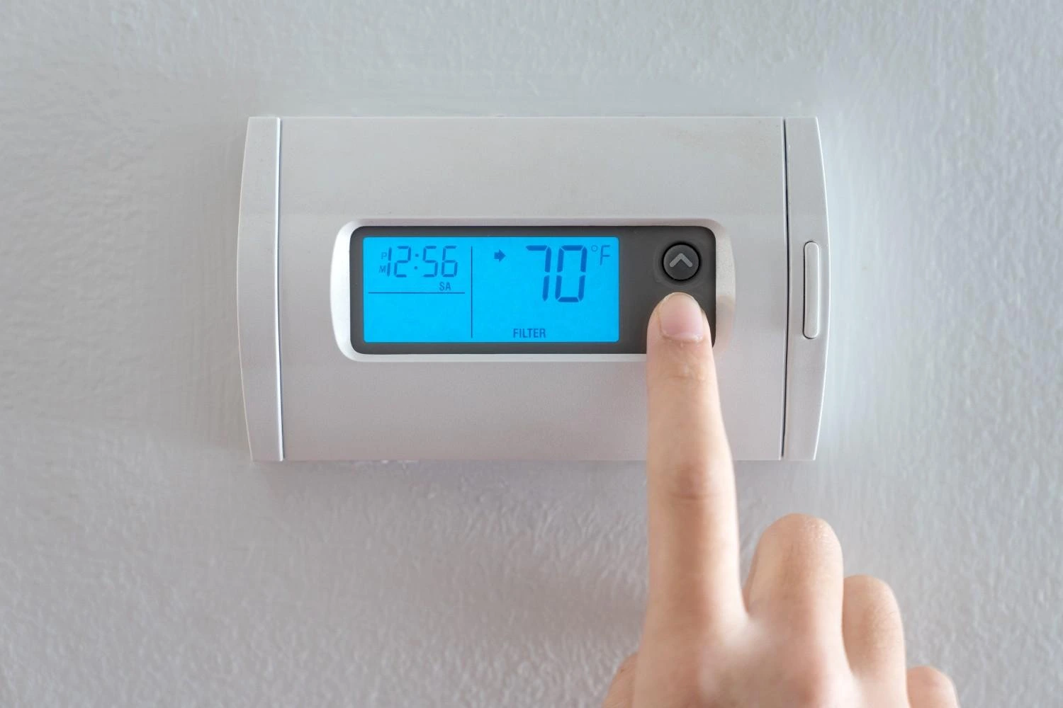 Person pressing the up arrow on a digital wall-mounted HVAC control panel explaining what does AUX heat mean for home temperature settings.