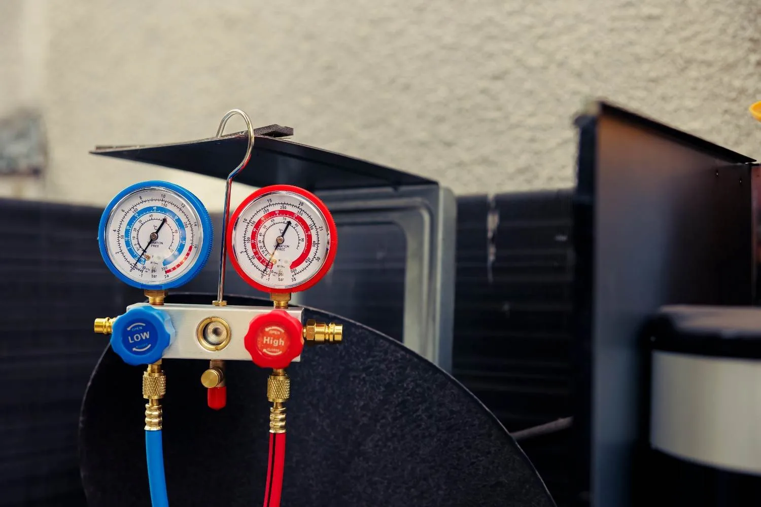 A close-up of blue and red refrigerant manifold gauges hooked up to an outdoor air conditioning unit, illustrating how technicians measure performance to explain what does SEER mean in HVAC systems.