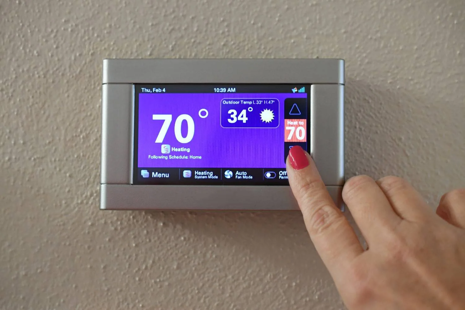 Finger tapping the touchscreen panel to illustrate what is AUX heat on a thermostat when indoor heating settings are adjusted during cold outdoor temperatures.