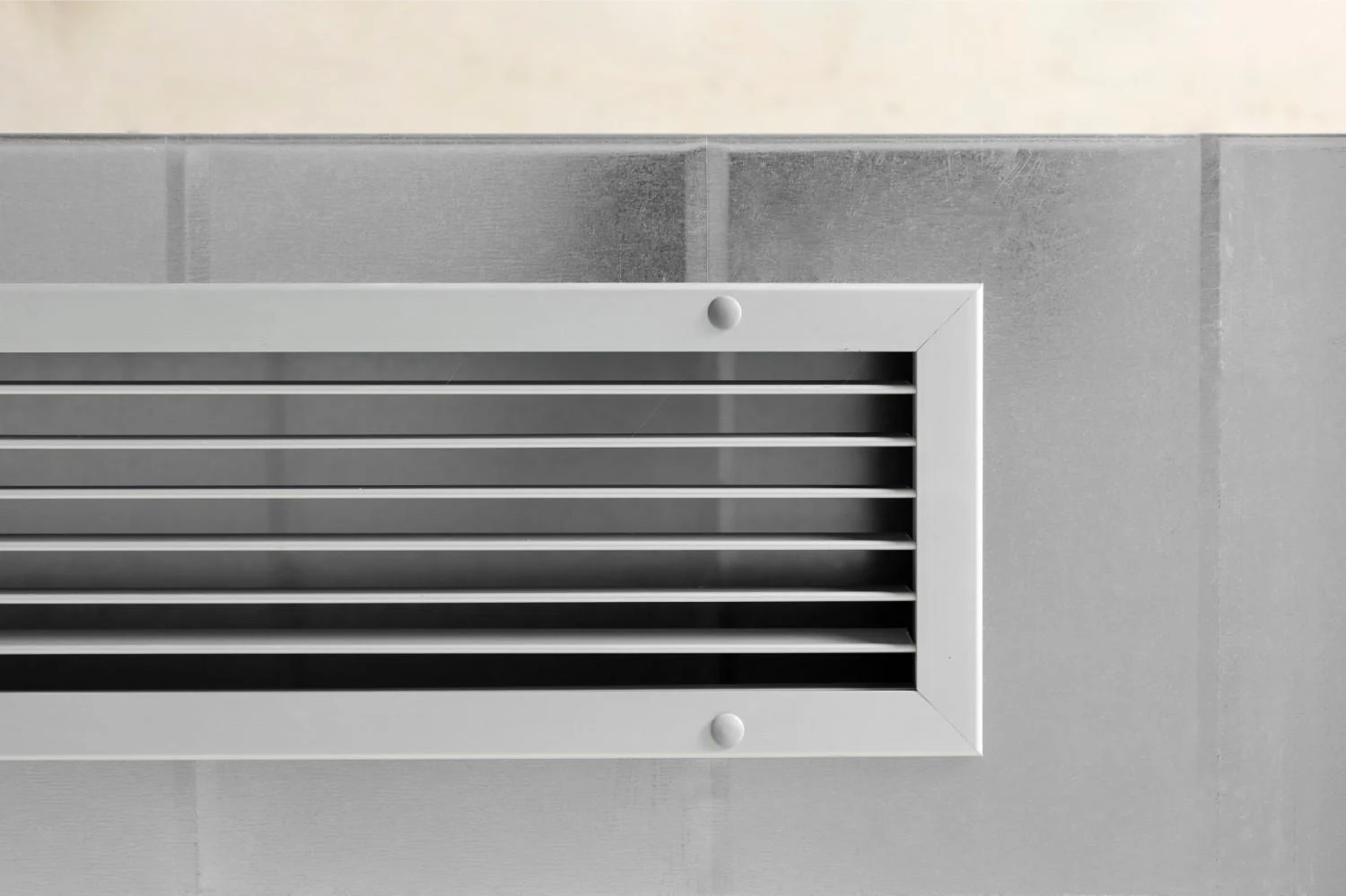 A close-up of a modern white HVAC air ventilation grille on a metallic duct system, illustrating where are HEPA filters used to clean indoor air.