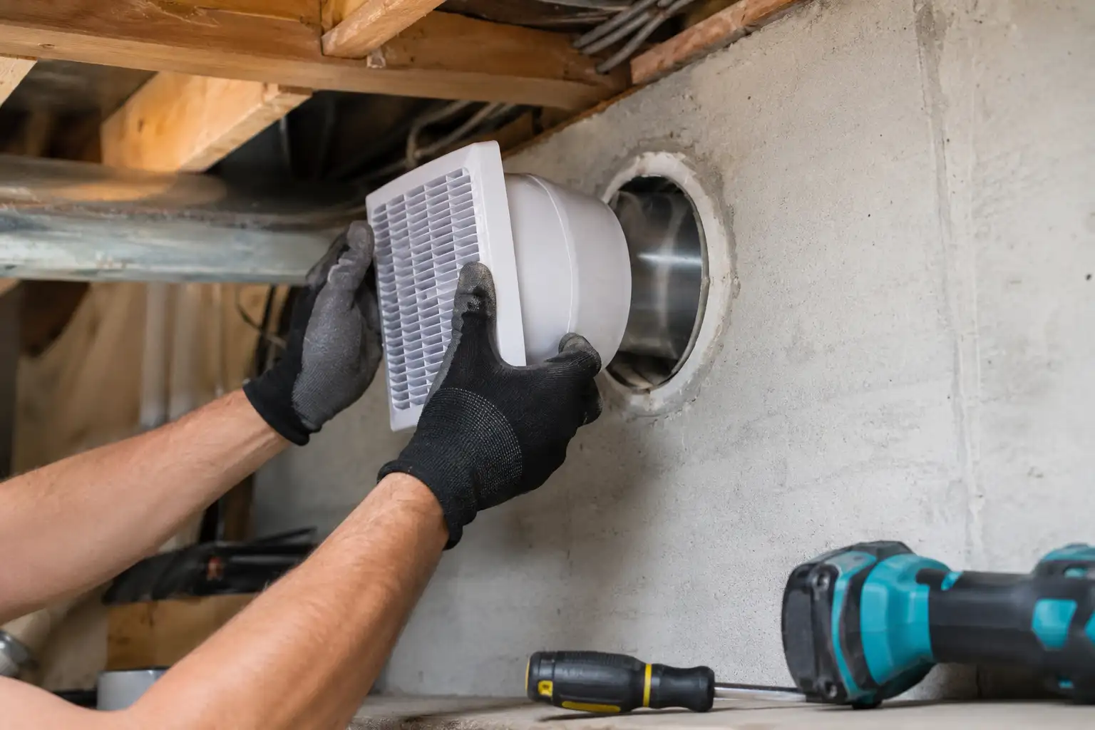 Technician installing a wall-mounted exhaust fan explaining why does a windowless basement need ventilation.
