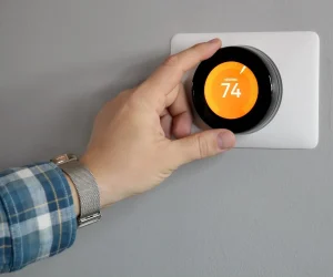 A man's hand adjusting a smart thermostat on a wall, illustrating the question: can nest thermostat