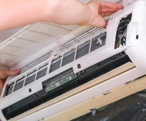 A technician opening the front panel of an indoor AC unit to troubleshoot common problems with mini