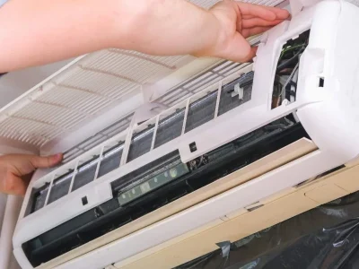 A technician opening the front panel of an indoor AC unit to troubleshoot common problems with mini splits.