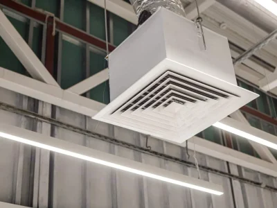 A close-up of a square grid supply ventilation duct in a commercial ceiling, illustrating the airflow mechanics behind how does an air purifier work to circulate clean air.