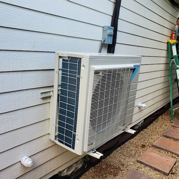 Wall-mounted mini split outdoor condenser unit beside home siding